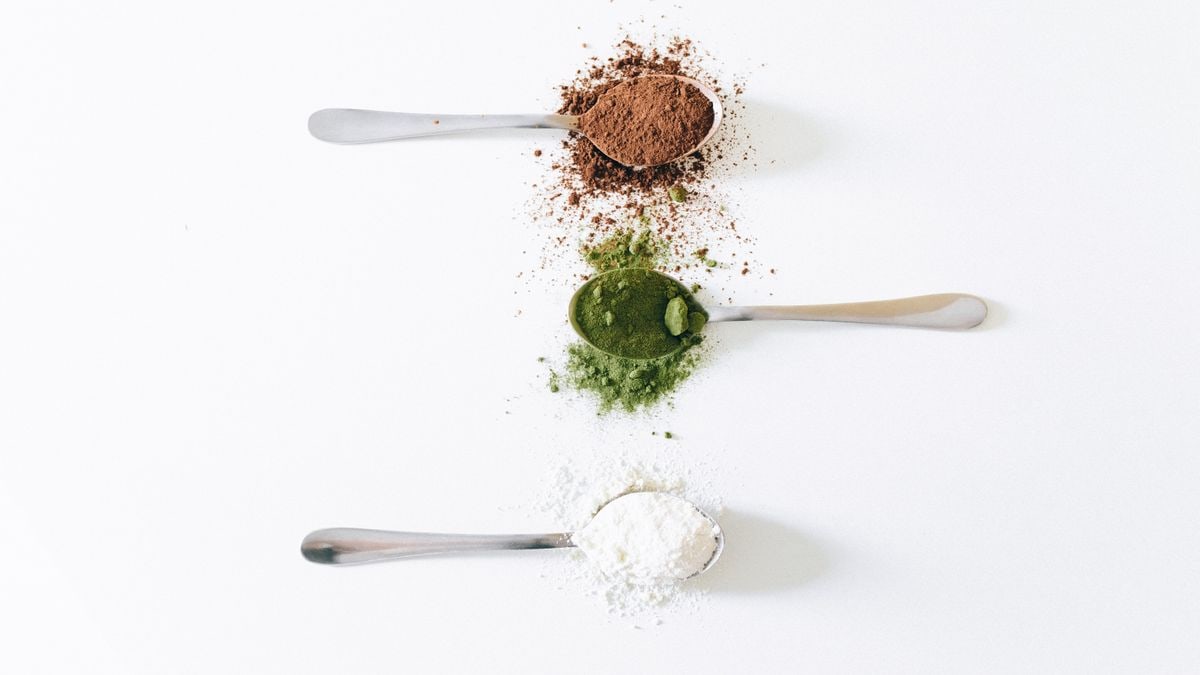 Top view of colorful assorted powders on spoons against white background.